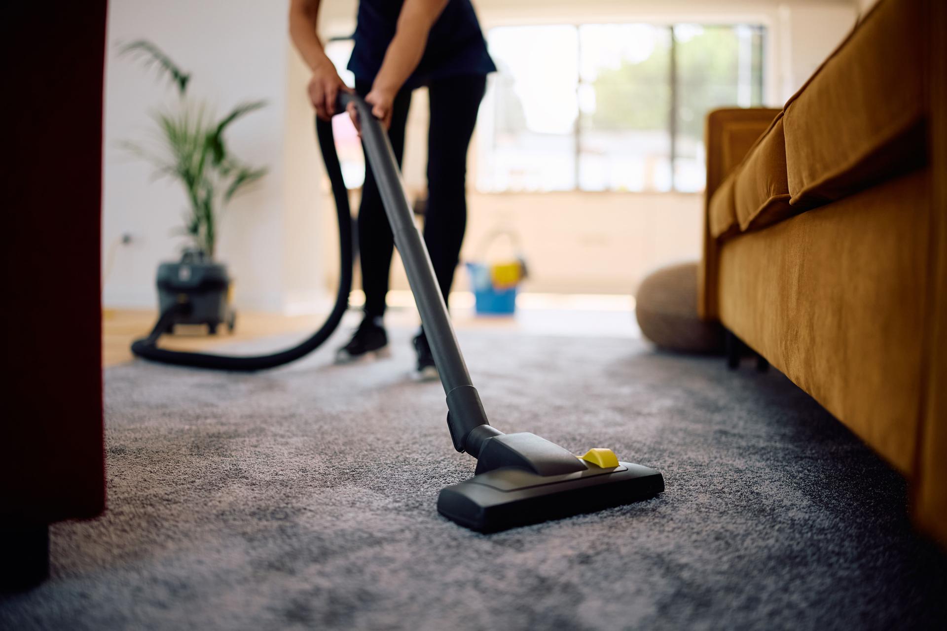 Close up of woman using vacuum cleaner while cleaning the apartment.